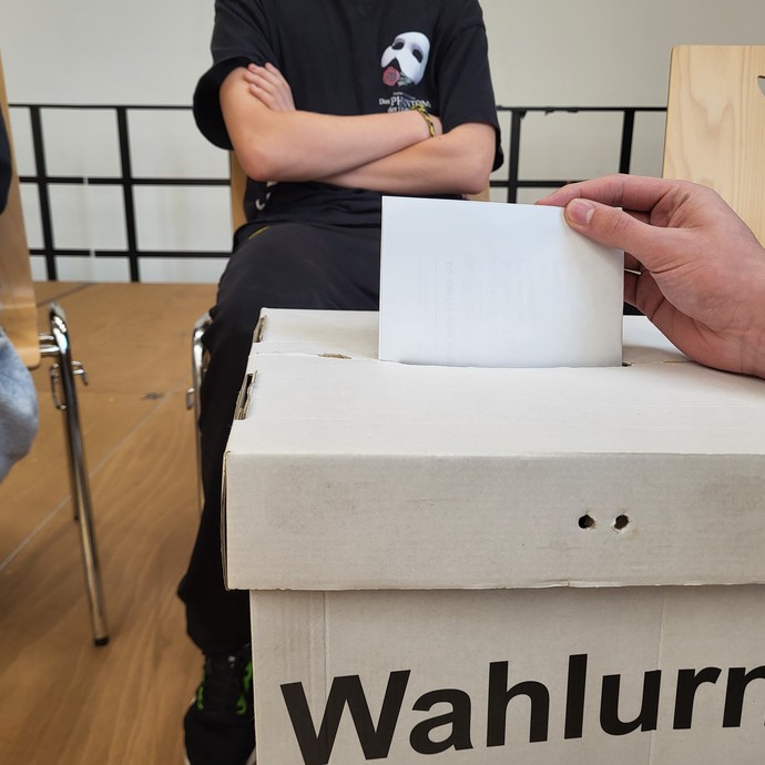 Nahaufnahme des Einwurfes eines Wahlzettels (vergrößerte Bildansicht wird geöffnet)