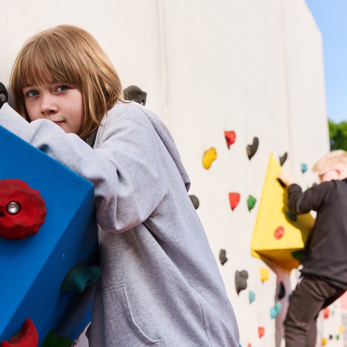 Eine Schülerin, die an an der Kletterwand klettert. Etwas entfernter klettert ein Schüler. (vergrößerte Bildansicht wird geöffnet)