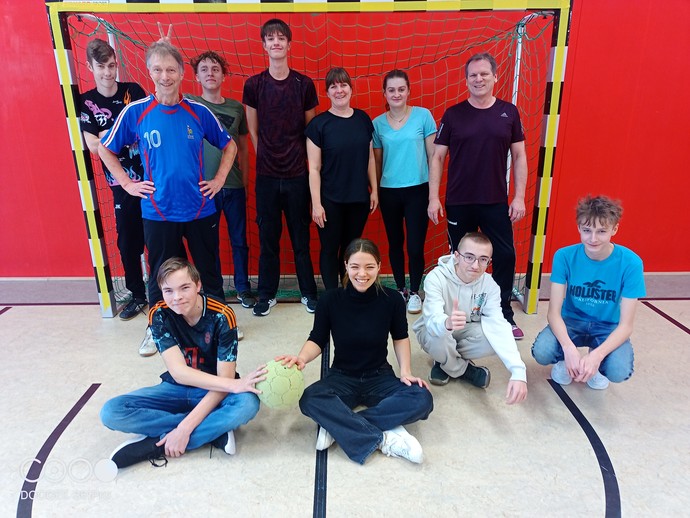 Einige Schülerinnen und Schüler sitzen und stehen vor einem Tor in der Turnhalle.