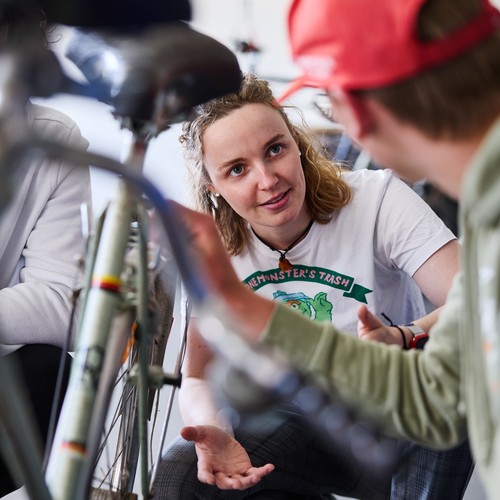 Werkstattleiterin Frau Klein repariert mit zwei Lernenden ein Fahrrad.