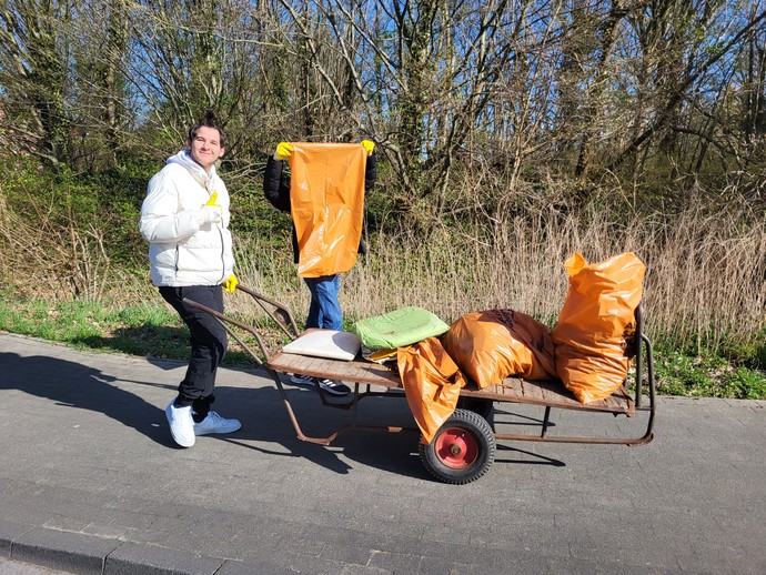 Ein Schüler schiebt einen Wagen mit 3 gefüllten Müllbsäcken. Daneben läuft ein Schüler der einen leeren Müllsack vor sich hoch hält.