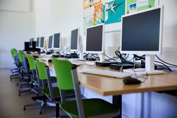 Eine Reihe von Monitoren und grünen Stühlen im Computerraum