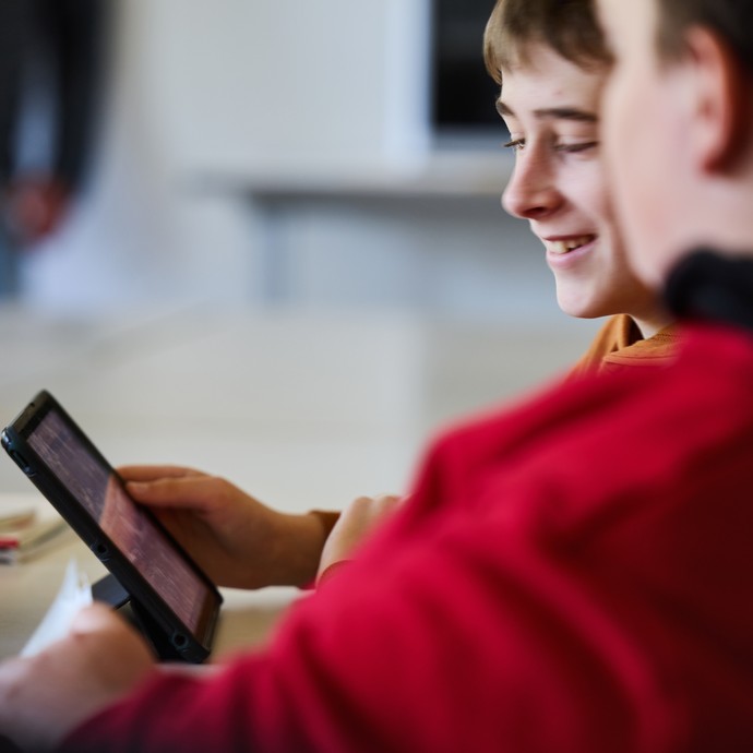 Zwei Schüler schauen auf ein Tablet. (vergrößerte Bildansicht wird geöffnet)