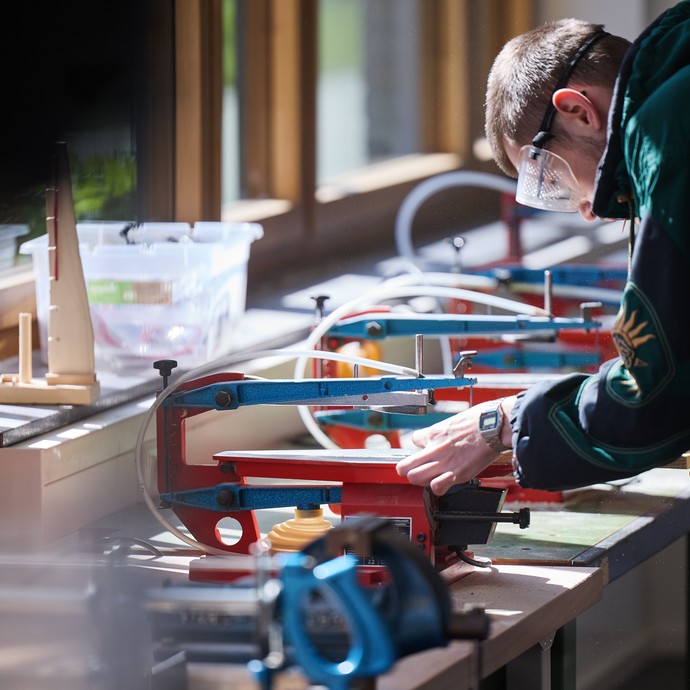 Eine Person mit Schutzbrille zersägt etwas. (vergrößerte Bildansicht wird geöffnet)