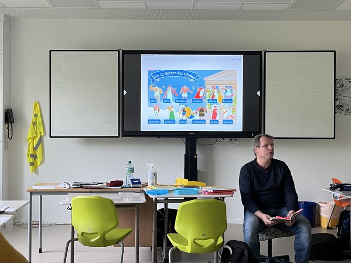 Herr Duddek liest am Pult. Hinter ihm ist ein Bildschrimpräsentation zu sehen.