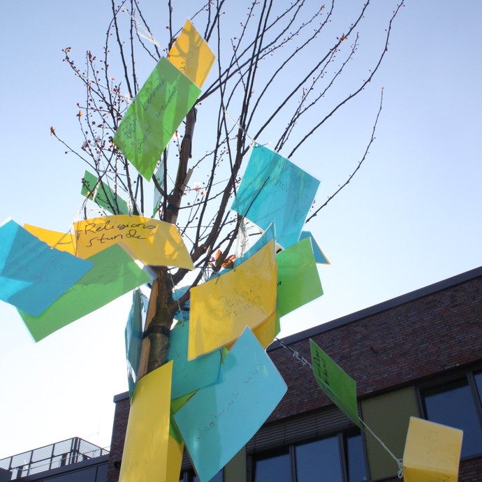 Ein Baum, an dem bunte Zettel befestigt sind, auf denen etwas steht. (vergrößerte Bildansicht wird geöffnet)