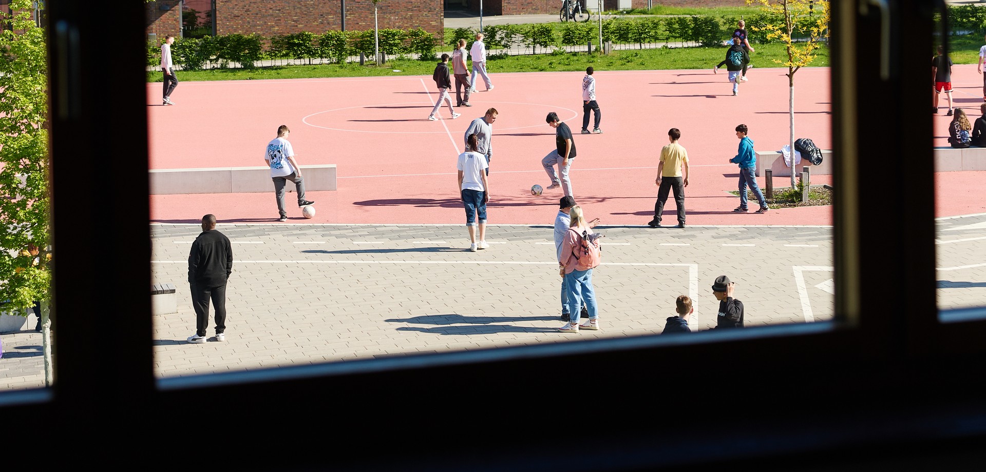 Blick aus dem Fenster zum Schulhof mit angrenzendem Sportplatz und einigen Lernenden