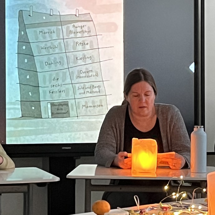 Eine Lehrerin liest am Pult vor einer stimmungsvollen Lampe. (vergrößerte Bildansicht wird geöffnet)