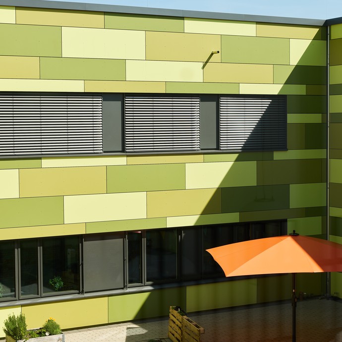 Ein Ausschnitt des grünen Schulgebäudes moit Sonnenschirm (vergrößerte Bildansicht wird geöffnet)