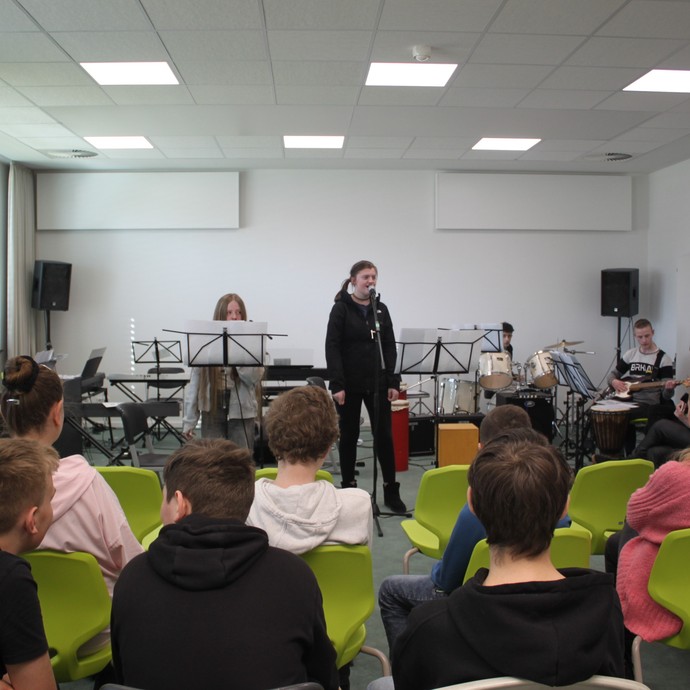 Die Schulband spielt vor einem Publikum in einem Klassenraum. (vergrößerte Bildansicht wird geöffnet)