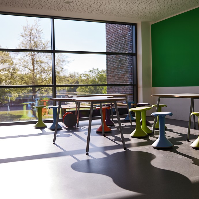 Ein Zimmer mit großer Fensterfront, Tischen und bunten Sitzhockern (vergrößerte Bildansicht wird geöffnet)