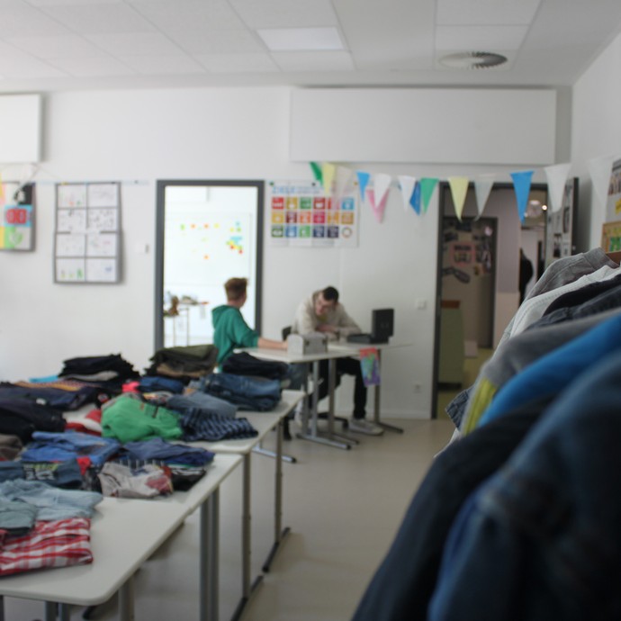 Ein dekoriertes Klassenzimmer mit einigen Personen und Hemden auf Tischen und aufgehängten Jacken (vergrößerte Bildansicht wird geöffnet)