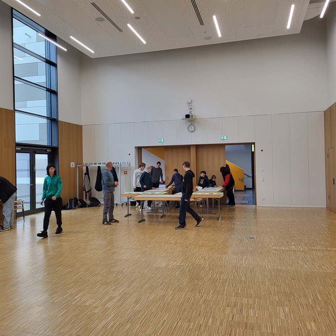 Wahlraum und Tisch mit Wahlurne und Lernenden, die die Wahl begleiten und Wählende. (vergrößerte Bildansicht wird geöffnet)