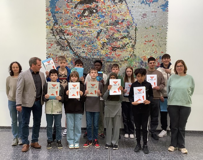 Schulleitung, zwei Lehrkräfte und zwölf Lernende stehen mit ihren Urkunden in der Hand vor dem Martin Luther Portrait.