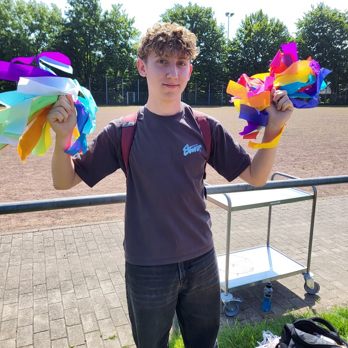 Ein Lernender hält bunte Papierpompons in die Luft. (vergrößerte Bildansicht wird geöffnet)