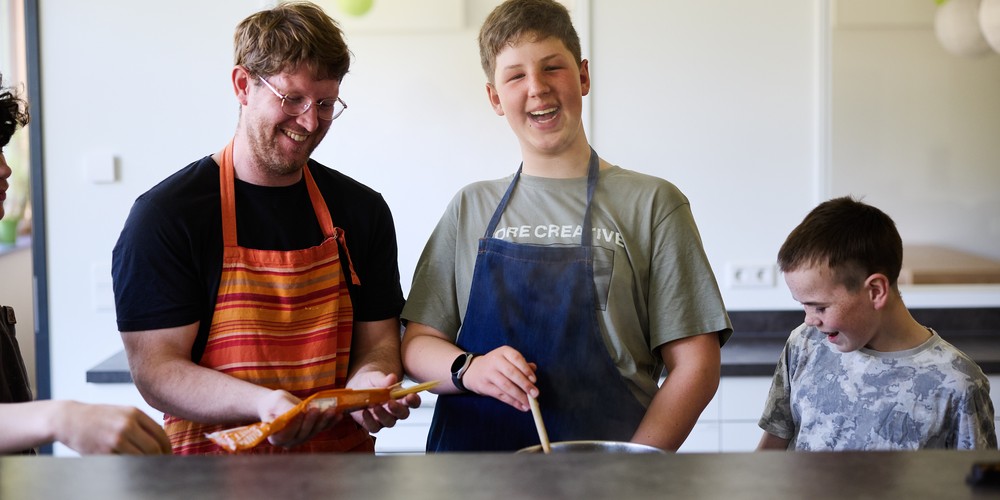 Drei Schüler lachen und einer von Ihnen rührt jeweils einen Kochtopf um.